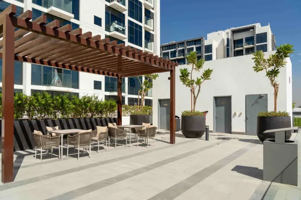 Outdoor patio area with tables and chairs under a wooden pergola, large potted plants, and modern apartment buildings in the background—ideal for future-proofing commercial properties with stylish, functional outdoor spaces.