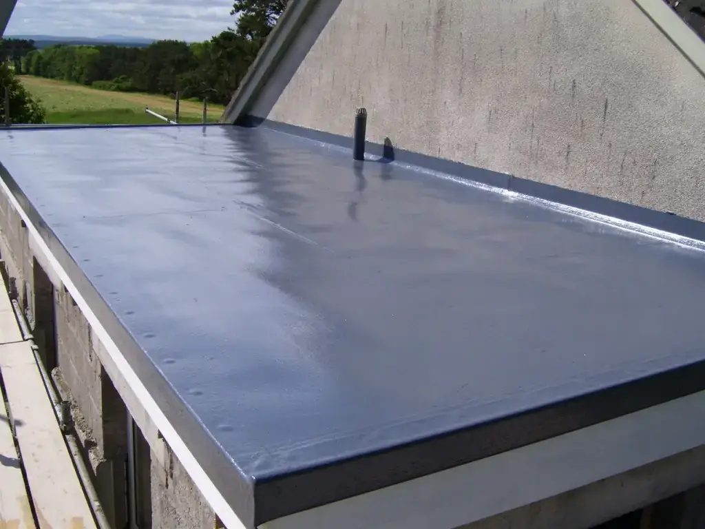 A flat roof with a smooth, shiny grey waterproof coating on top of a building, recently completed as part of a roof replacement project, surrounded by countryside.