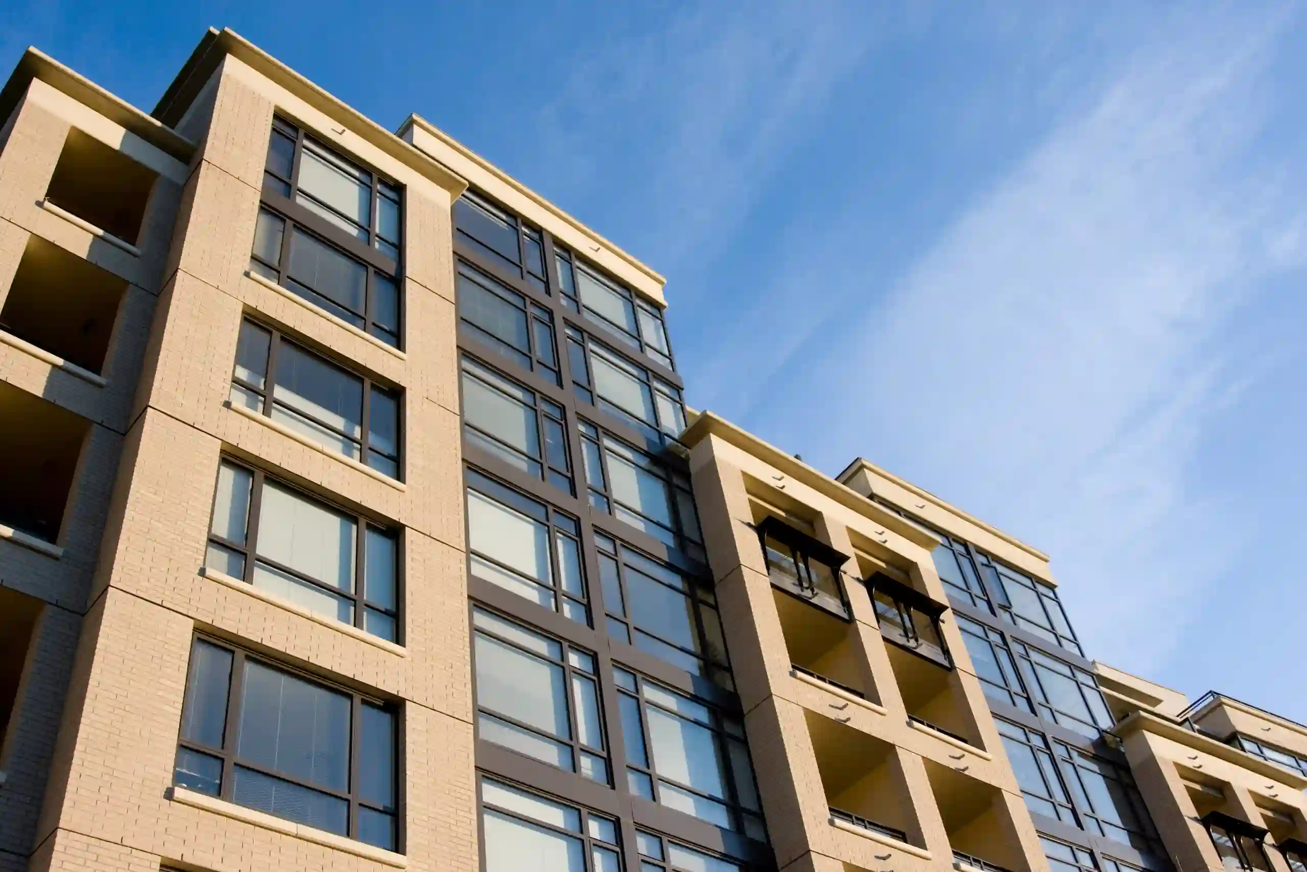 View of a modern apartment building with large windows and balconies under a clear blue sky, seen from a low angle.