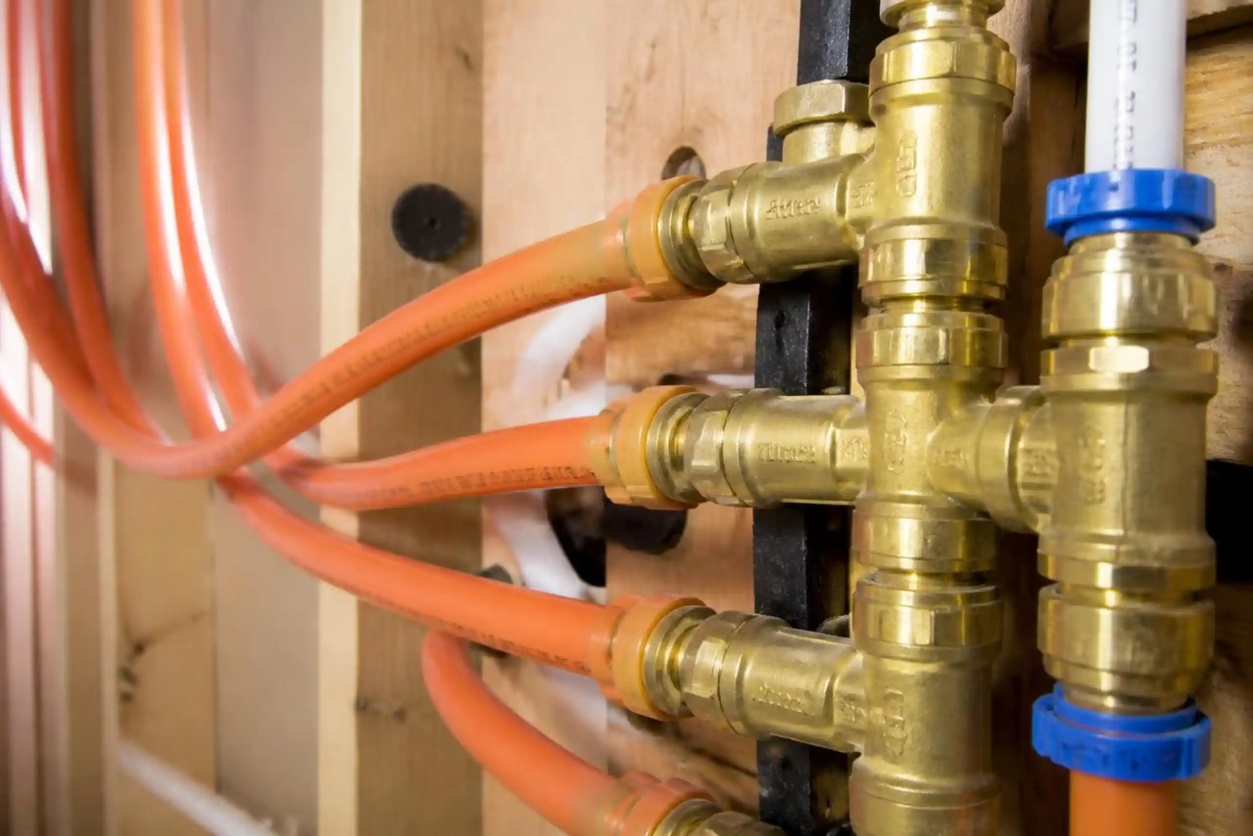 Close-up of orange PEX water pipes connected to brass manifold fittings, installed on a wooden frame, part of a plumbing system in a building under construction.