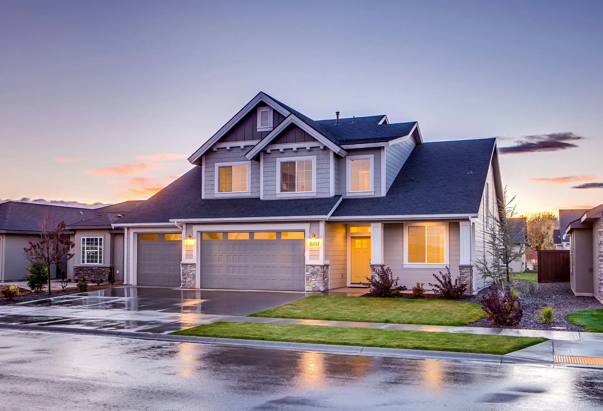 This large two-story house in Coquitlam boasts a well-lit exterior with a three-car garage, manicured lawn, and wet pavement under a twilight sky. Recent pipe replacement ensures modern functionality alongside its charming appeal.