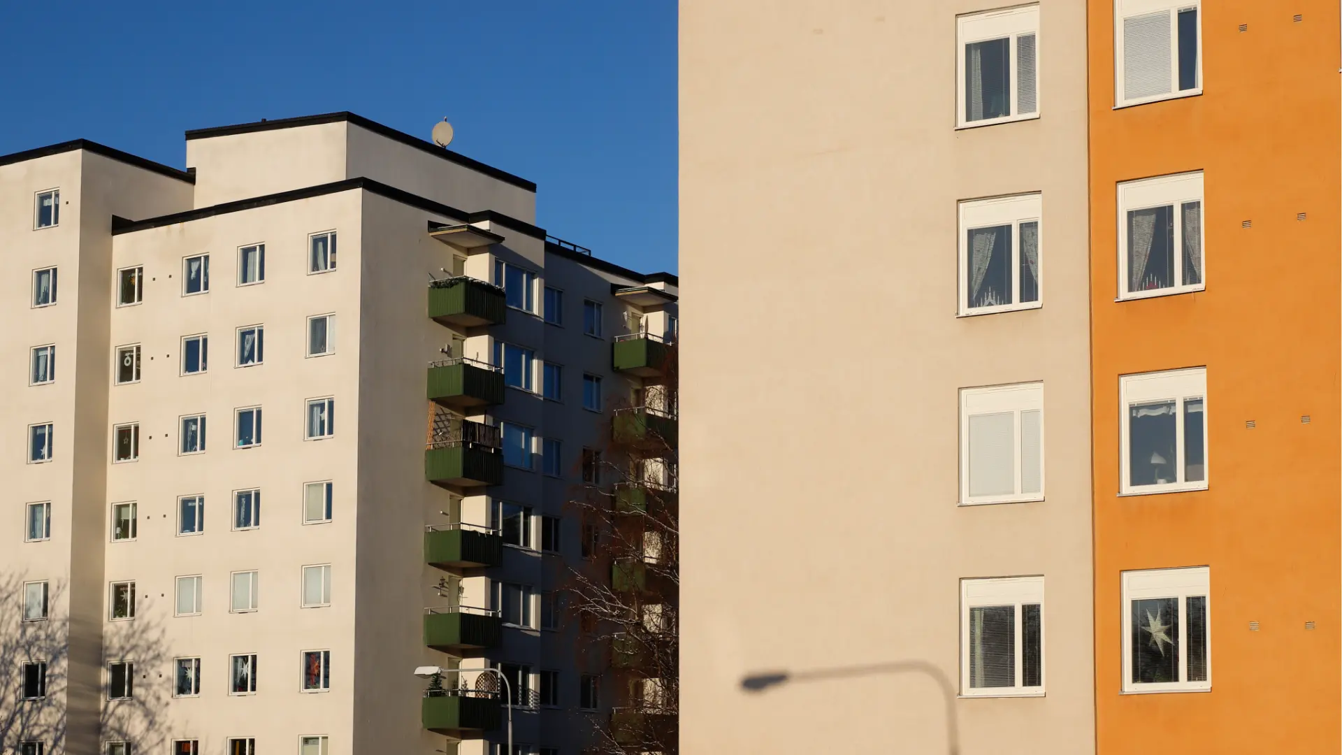 Under a clear blue sky in Abbotsford, two apartment buildings stand side by side. One is a white multi-unit property with green balconies, while the other boasts a beige exterior accented by an orange section and white-framed windows.