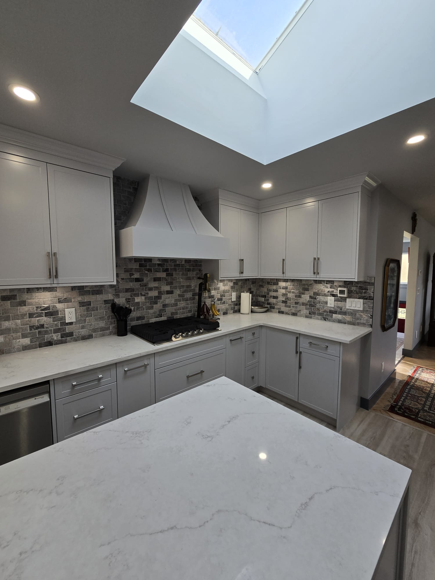 Modern kitchen with white cabinets, marble countertops, gray tile backsplash, stainless steel appliances, and a skylight providing natural light—designed for easy property maintenance and lasting appeal.