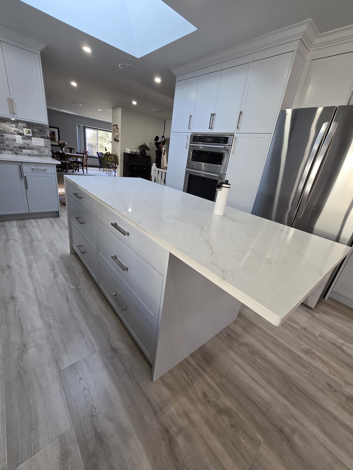 Modern kitchen with light gray cabinets, large marble island, stainless steel appliances, and light wood flooring; a white water bottle sits on the island, showcasing the care and attention to property maintenance throughout.