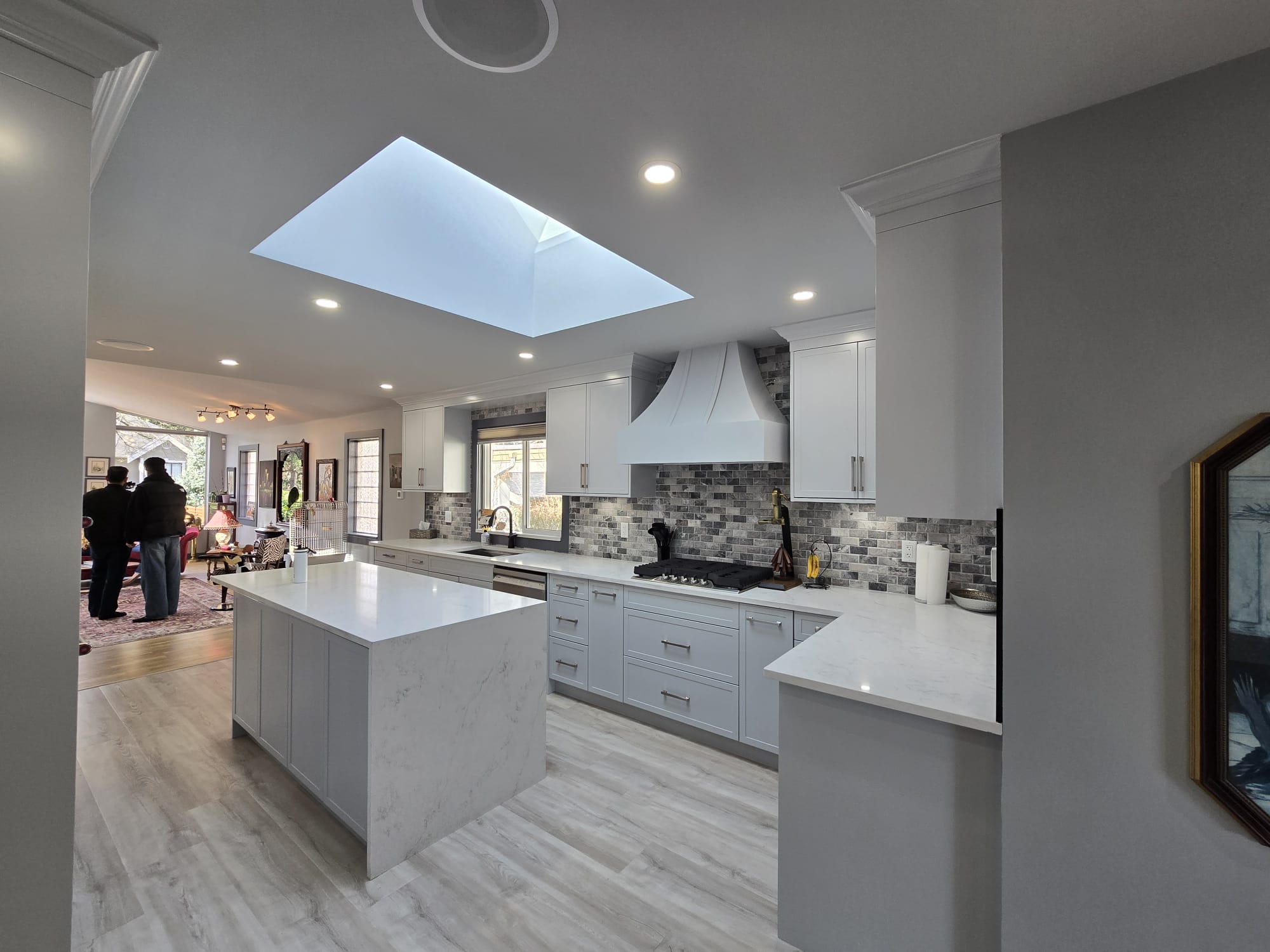 Modern kitchen with white cabinets, marble island, and a skylight; two people are seen standing in the adjacent living area, highlighting the benefits of attentive property maintenance.