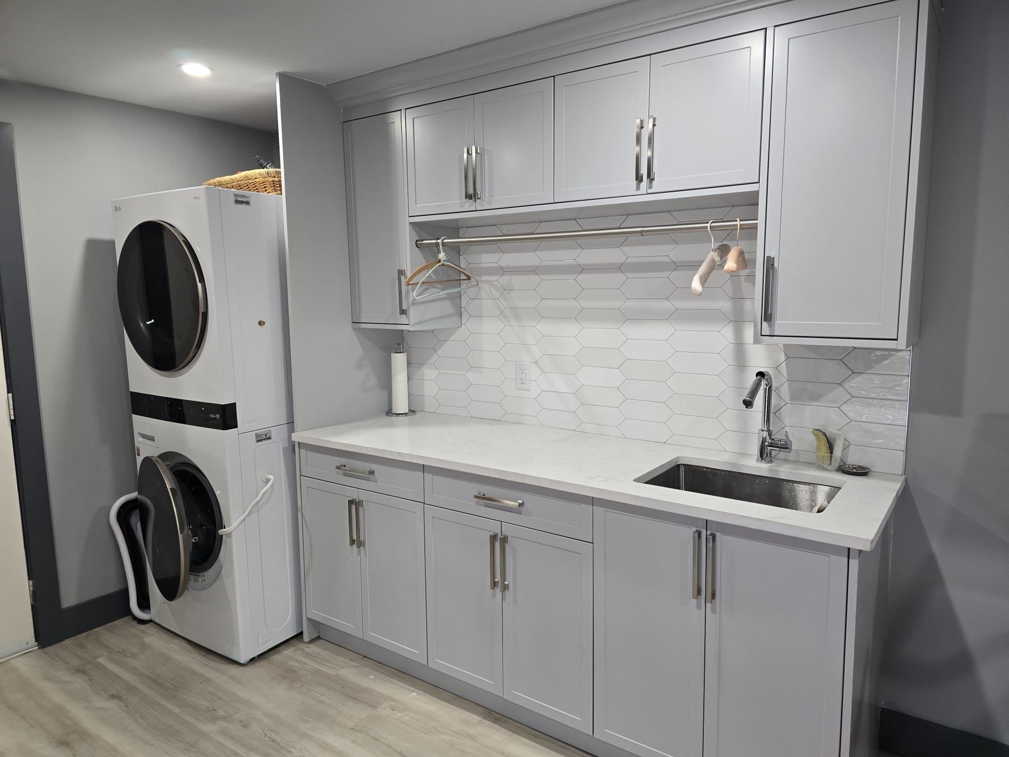 Modern laundry room with stacked washer and dryer, light gray cabinets, white hexagon tile backsplash, and a stainless steel sink—ideal for easy property maintenance.