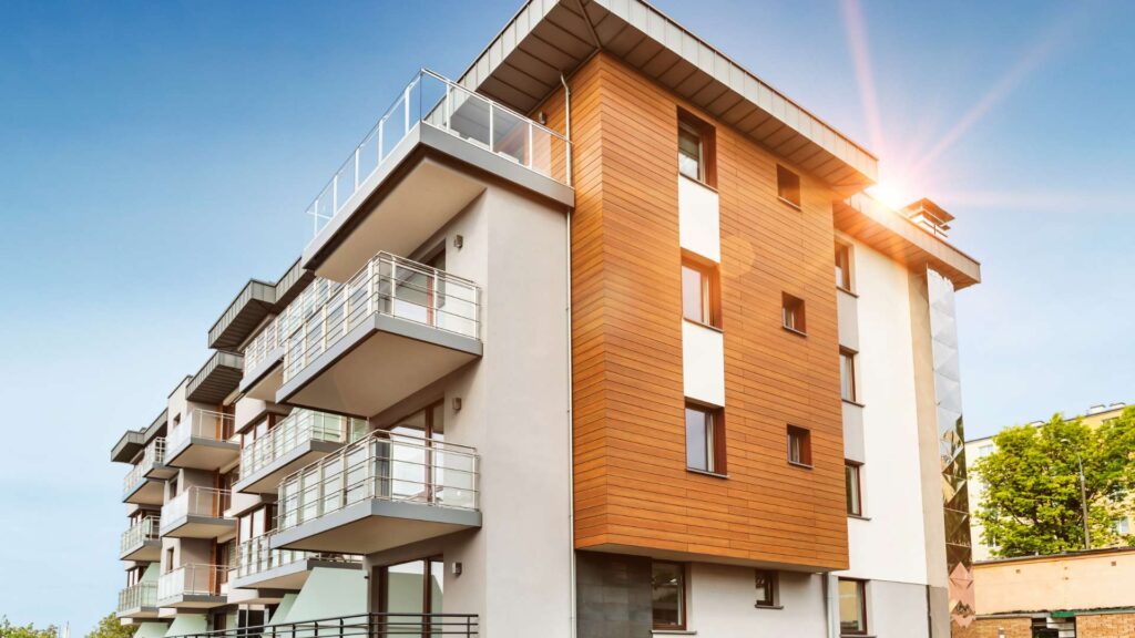 Modern apartment building with balconies, featuring a combination of white and wooden paneling under a clear blue sky with sunlight, showcasing expert flooring installation throughout.